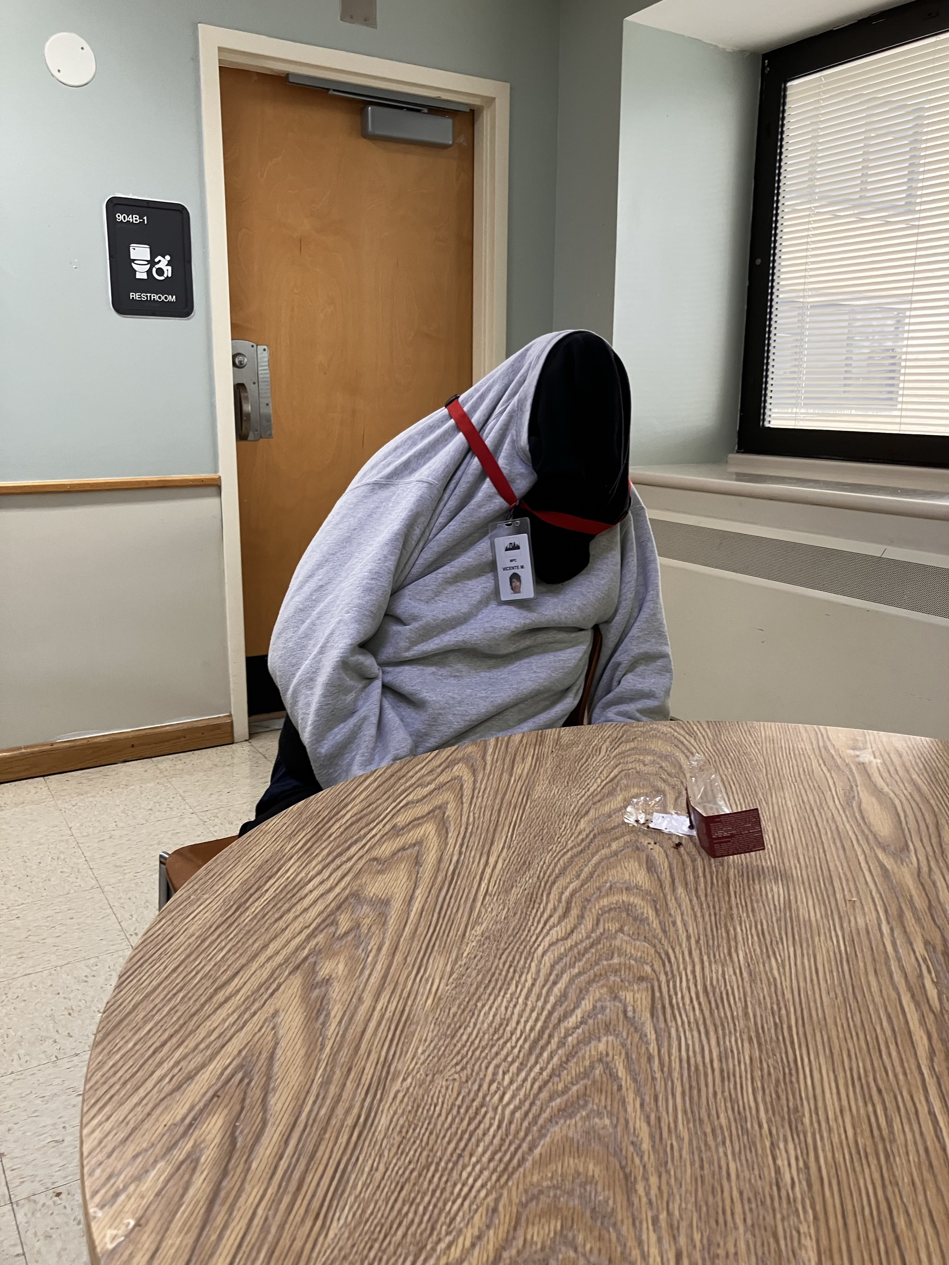 A person hidden inside a sweatshirt seated at a table