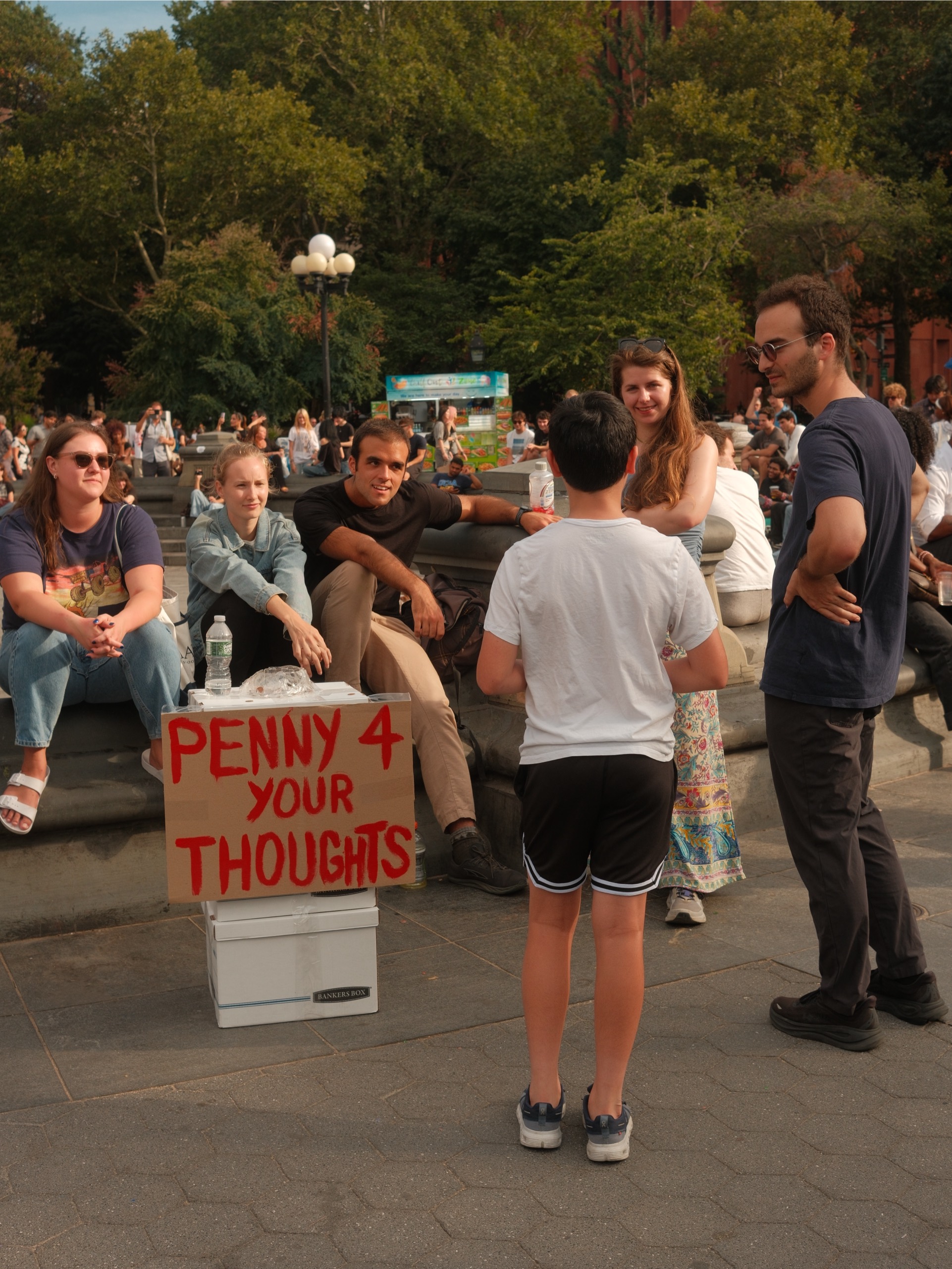 People gathered in a park beside a Penny 4 Your Thoughts sign