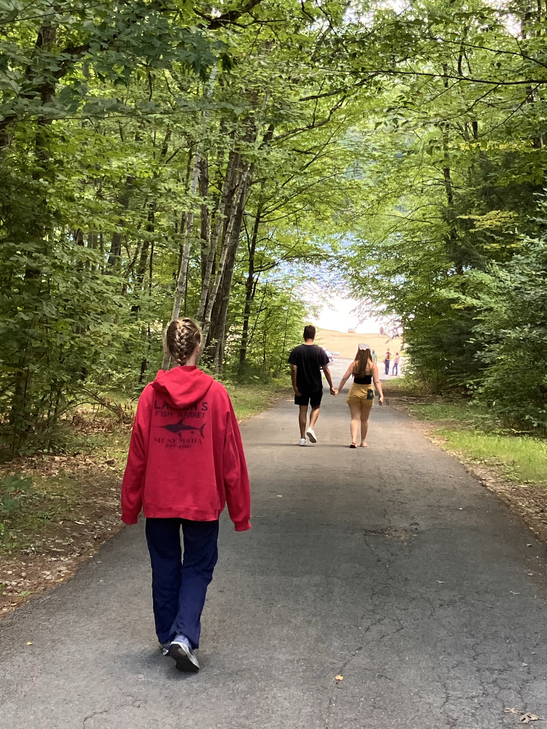 People walking along a tree-lined path toward the water