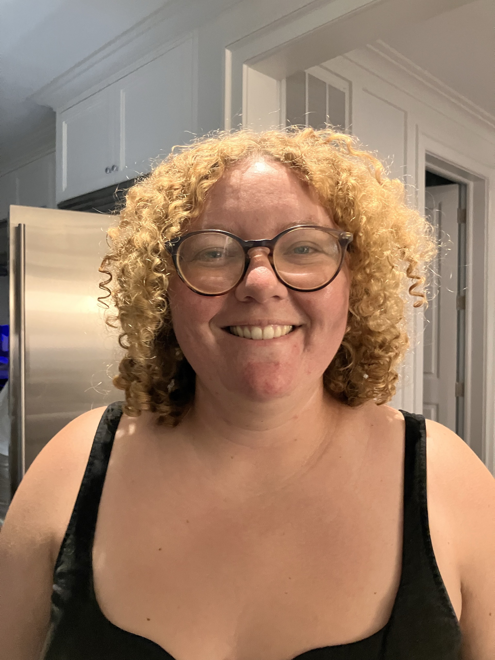 Smiling person with curly hair and glasses